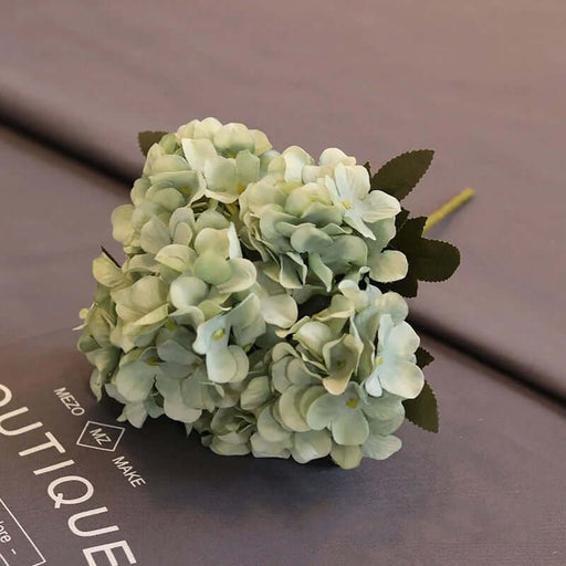 Light Green hydrangea flower arrangement on a brown surface with text