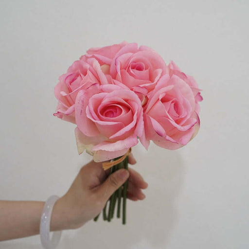 Hand holding a bouquet of artificial pink latex snow mountain roses, perfect for event decor.