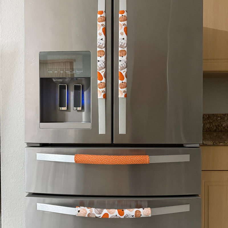 Four stainless steel refrigerator handles covered in orange and white patterned fabric sleeves featuring cartoon pumpkins, shown on a refrigerator in a kitchen setting.