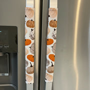 Two fabric refrigerator door covers with an autumn pumpkin pattern, shown on the handles of a stainless steel refrigerator.