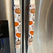 Two refrigerator handle covers with a fall harvest pumpkin and acorn pattern, shown on stainless steel refrigerator handles.