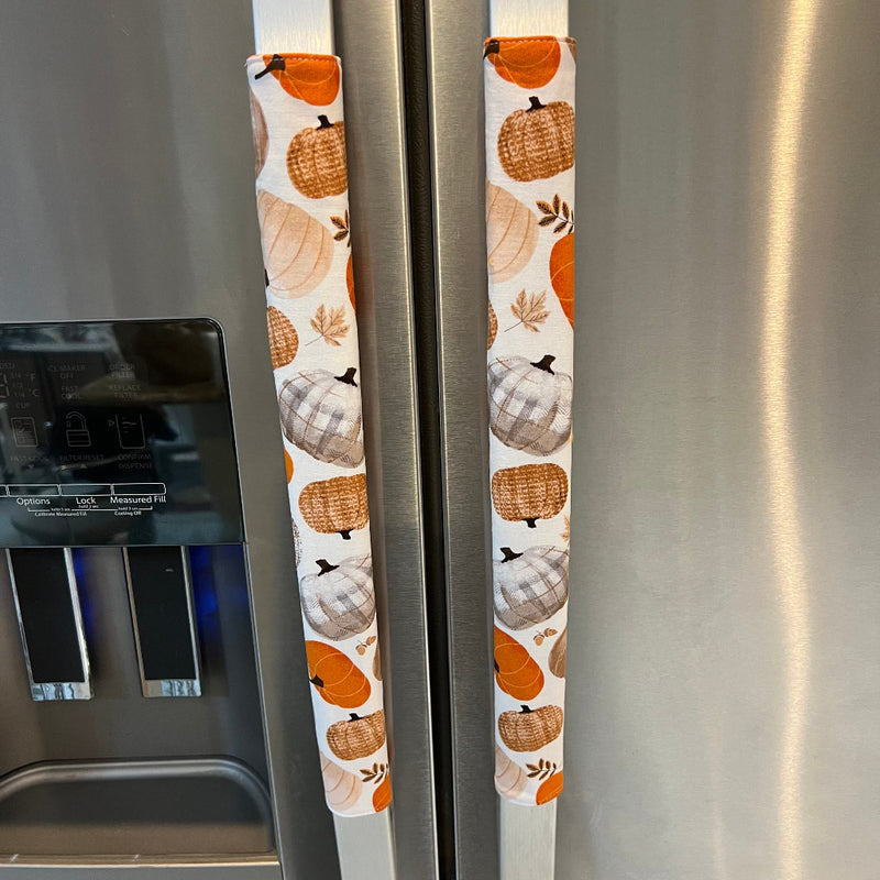  Refrigerator handles covered in fabric handles featuring an autumn pumpkin pattern in orange, brown, and beige, installed on a stainless steel refrigerator.