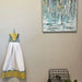 Handmade kitchen towel with a blue and yellow design hanging on a wall beside an abstract painting and a plant.