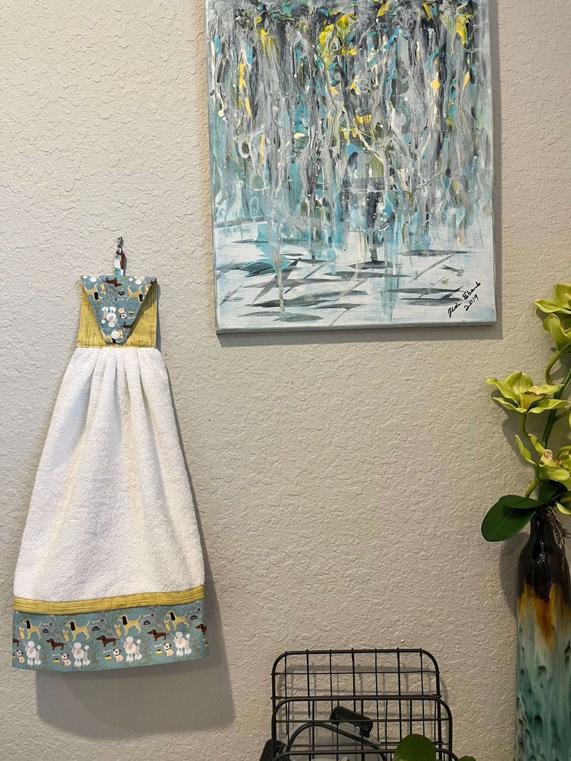 Handmade puppy print kitchen towel hanging on wall next to abstract artwork and a decorative vase.