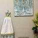 Handmade puppy print kitchen towel hanging on wall next to abstract artwork and a decorative vase.