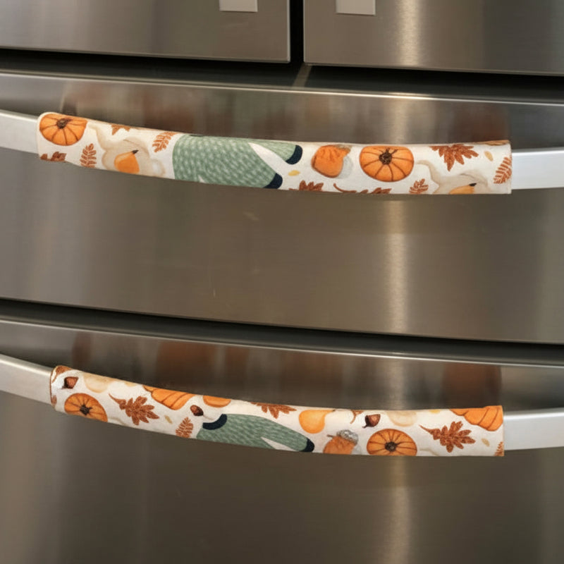 A stainless steel refrigerator with decorative fabric handle covers in a fall harvest pattern.