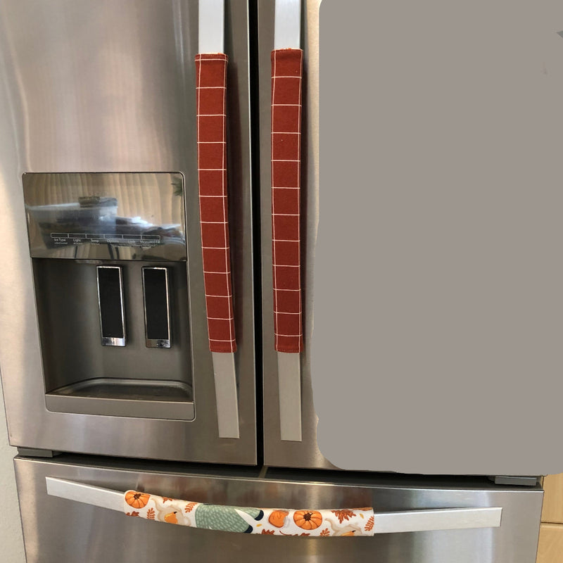 A stainless steel refrigerator with decorative fabric handle covers in a fall harvest pattern, 