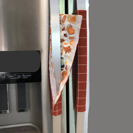 A stainless steel refrigerator with decorative fall theme  handle covers showing the flip side.