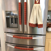 A stainless steel Whirlpool French-door refrigerator in a kitchen setting, decorated with three red-and-white checkered towel handles hanging on the handles and door.