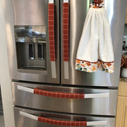 A stainless steel Whirlpool French-door refrigerator with decorative red-and-white striped and patterned handle covers, plus a white towel hanging on the right door handle in a kitchen setting.