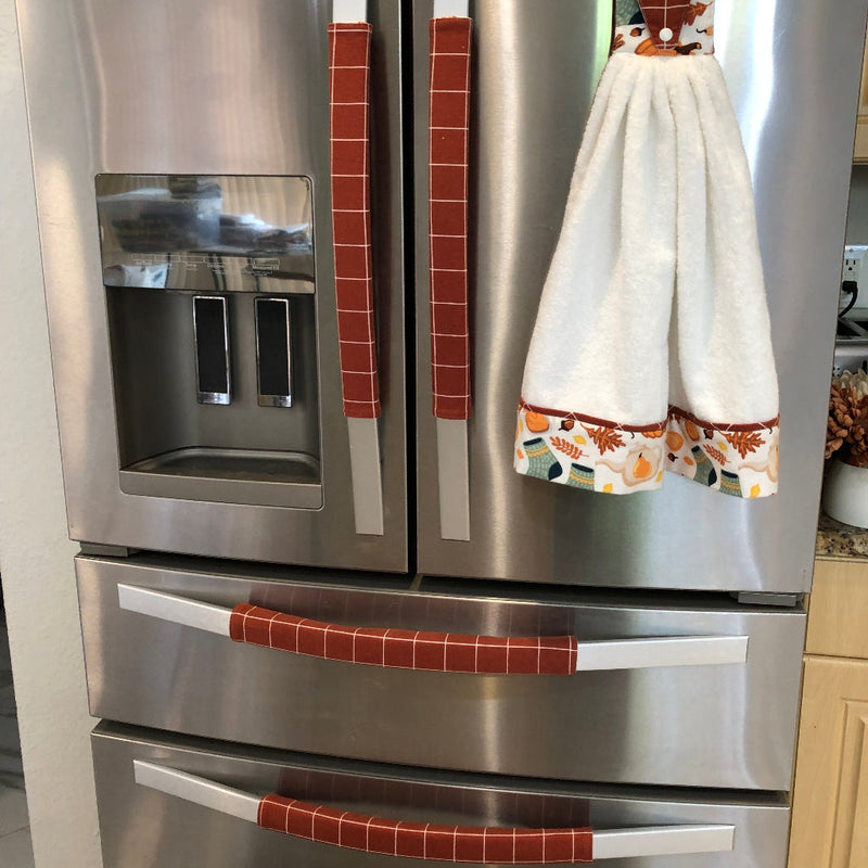 A stainless steel Whirlpool French-door refrigerator with decorative red-and-white striped and patterned handle covers, plus a white towel hanging on the right door handle in a kitchen setting.