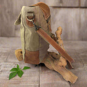 Eco-friendly khaki shoulder bag with tan leather flap showcased on a wooden surface with green leaves.