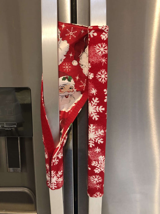 Festive red appliance handle cover with snowflakes and Santa design on a stainless steel fridge.