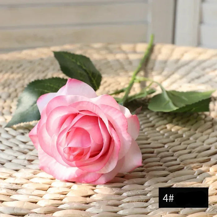 Latex real-touch artificial rose in soft pink hues resting on a woven surface, showcasing realistic details and vibrant colors.