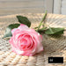 Latex real-touch artificial rose in soft pink hues resting on a woven surface, showcasing realistic details and vibrant colors.