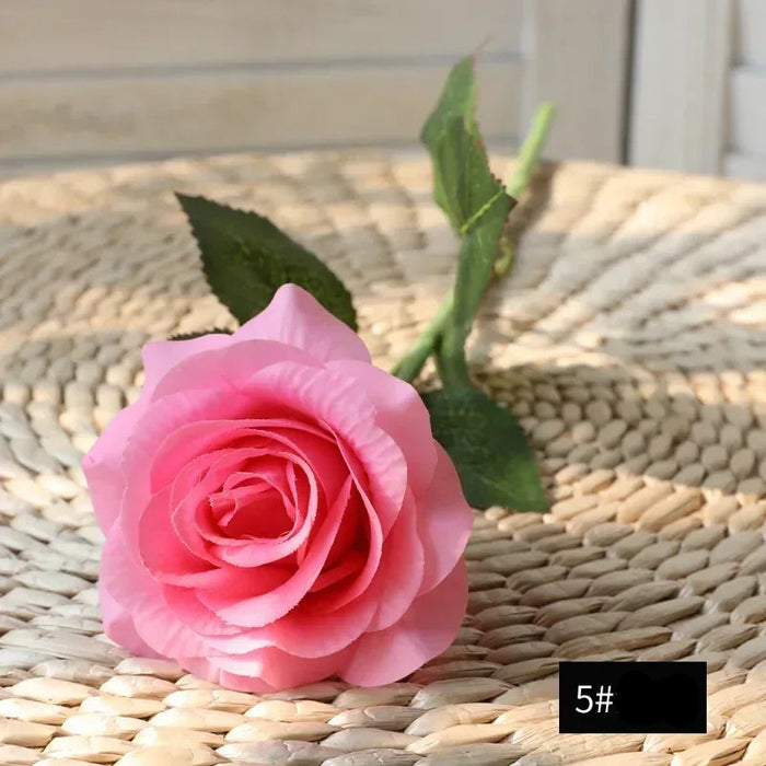 Latex real-touch artificial rose in pink color, showcasing its lifelike appearance and detailed petals on a woven background.