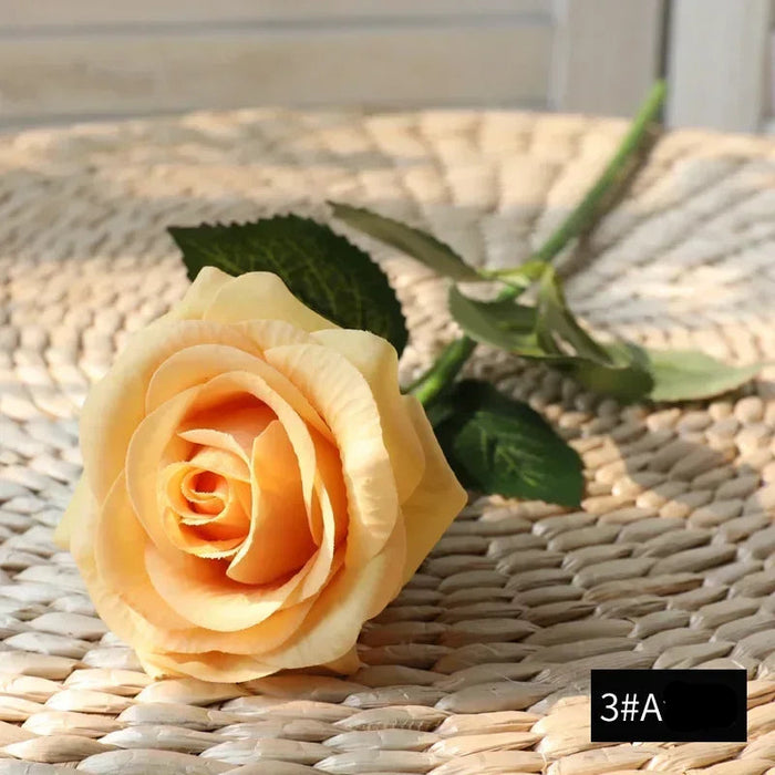 Latex real-touch artificial rose in champagne color resting on a woven surface.
