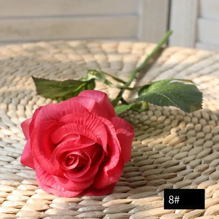 Latex real-touch artificial rose in coral color resting on a woven surface, showcasing its lifelike appearance.
