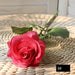 Latex real-touch artificial rose in coral color resting on a woven surface, showcasing its lifelike appearance.