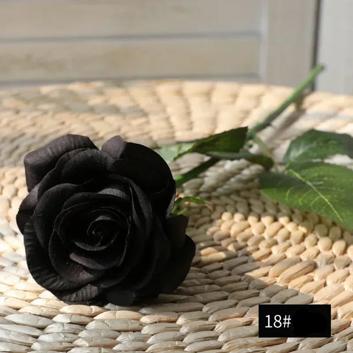 Latex real-touch artificial rose in black laying on a woven surface, showcasing realistic petal details.