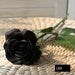 Latex real-touch artificial rose in black laying on a woven surface, showcasing realistic petal details.