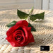 Latex real-touch artificial rose in full bloom on a woven surface, showcasing vibrant red petals and green leaves.