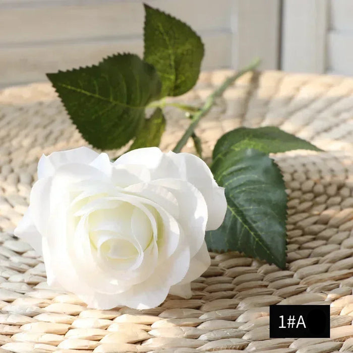 Latex real-touch artificial rose in white with green leaves on a woven basket surface.