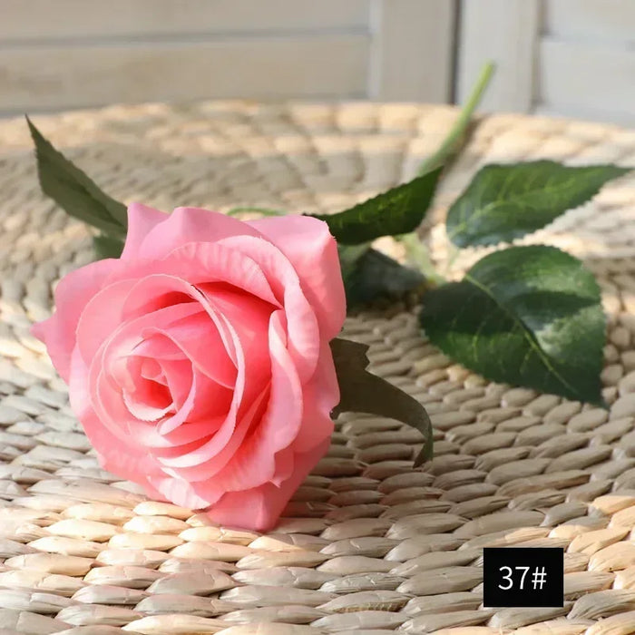 Latex real-touch artificial rose in pink color with green leaves on woven background.