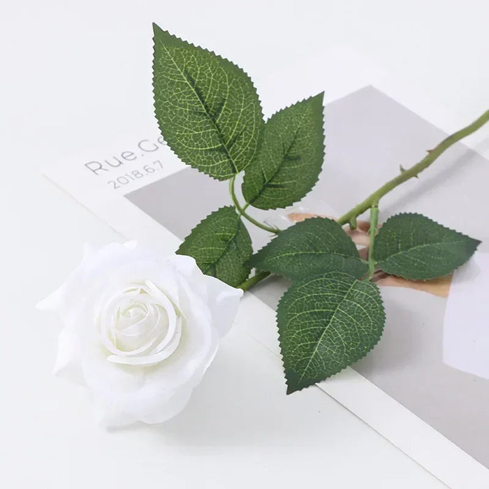 Latex real-touch artificial rose with white petals and green leaves on a magazine background.