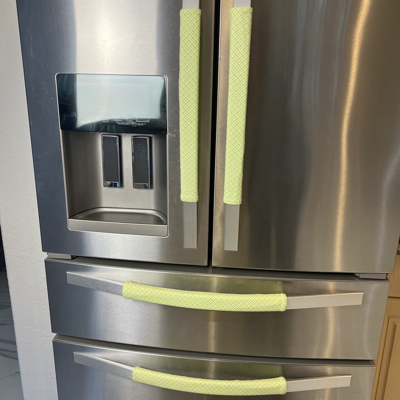 Stainless steel refrigerator with mint green handle covers in a kitchen setting.