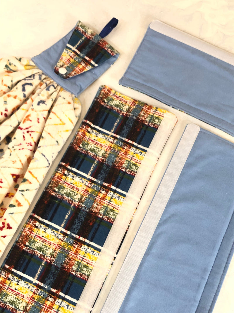 Plaid reversible light blue handle covers with a matching towel and colorful, patterned fabric on a white background.
