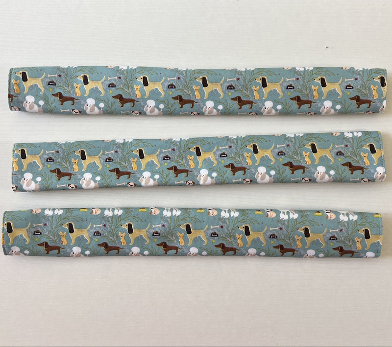 Three fridge handle covers with a blue-green background and a repeating pattern of dachshund dogs, white poodles, on a light beige surface.