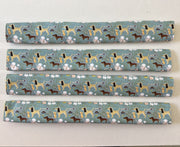 Four fridge handle covers with a repeating pattern of various dog breeds on a muted sage green background, displayed horizontally on a light wood surface.