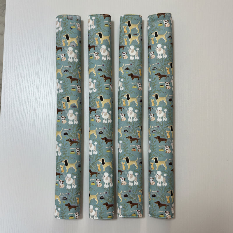 Four fridge handle covers with a repeating pattern of various dog breeds on a muted blue-green background, displayed vertically on a white surface.