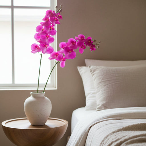Fuchsia artificial butterfly orchid on a table beside a bed 