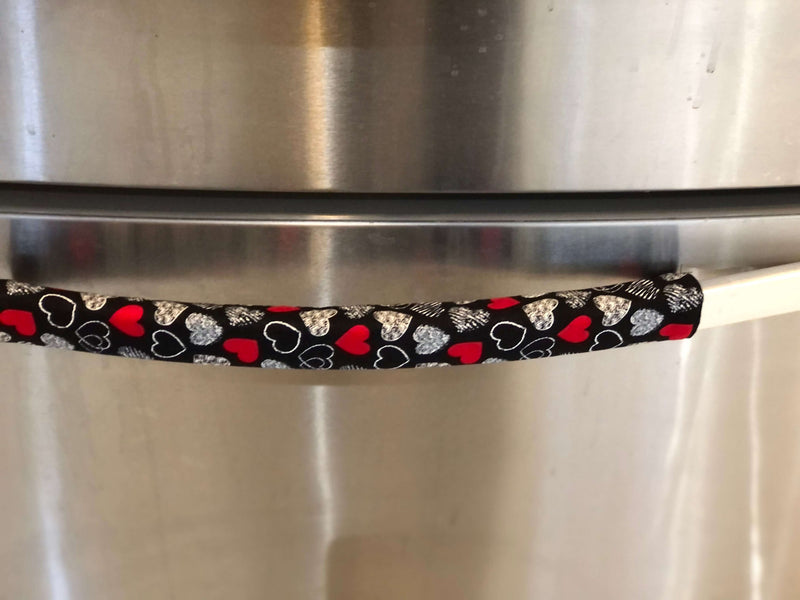 Red and white hearts on black Valentine-themed appliance handle covers on a refrigerator handle.