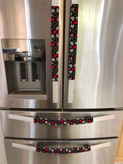 Red and white hearts on black Valentine-themed appliance handle covers on a stainless steel fridge.