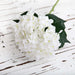 Realistic white Latex Hydrangea artificial flowers with green leaves on a rustic wooden surface.