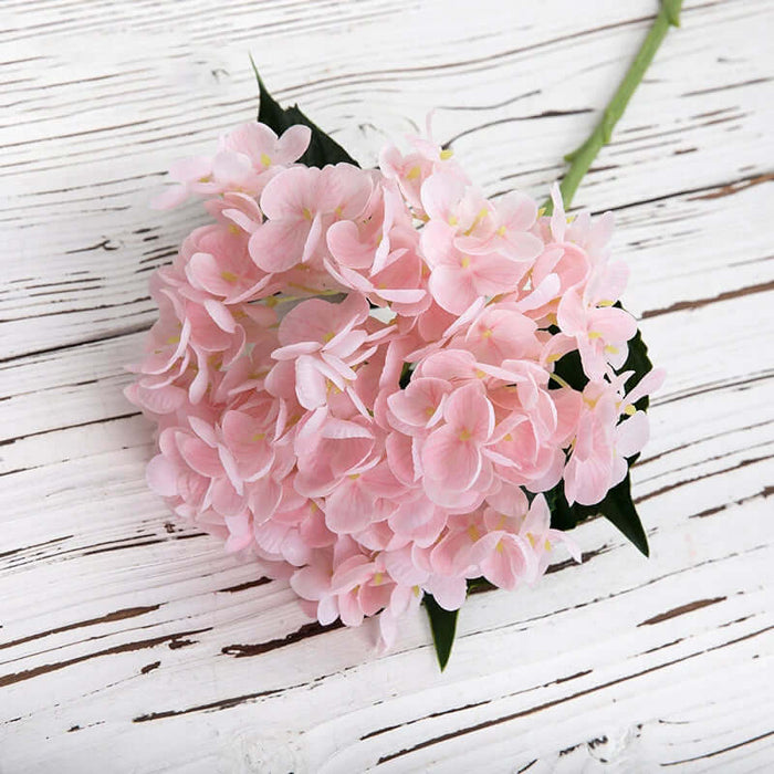 Pink Latex Hydrangea Real Touch Artificial Flowers with green leaves on distressed white wooden background.