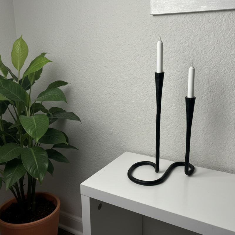 Black candle holder with two white candles on a white surface against a gray wall.