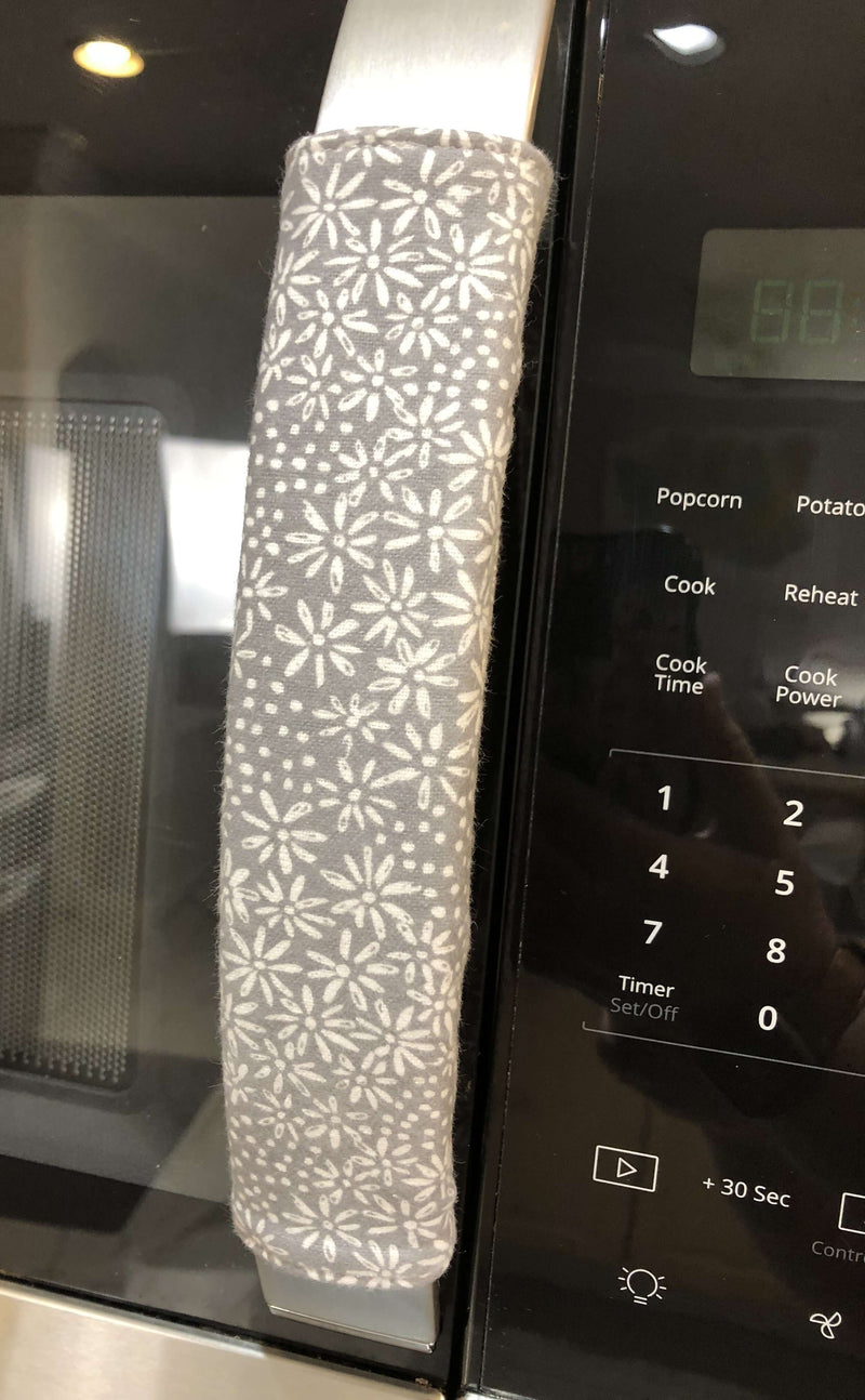 Grey and white gerbera daisy handle covers on a stainless steel refrigerator handle.
