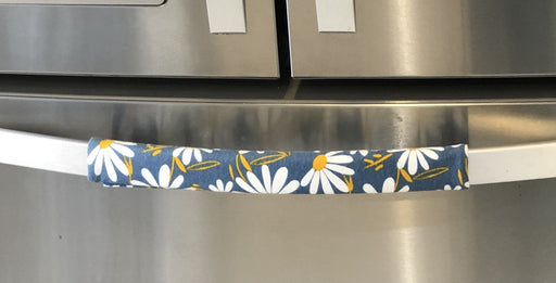 White and yellow daisy-patterned appliance handle cover on a stainless steel fridge handle.