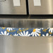 White and yellow daisy-patterned appliance handle cover on a stainless steel fridge handle.