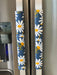 Decorative white and yellow daisy handle covers on blue appliance handles, enhancing kitchen style and protection.