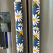 Decorative white and yellow daisy handle covers on blue appliance handles, enhancing kitchen style and protection.