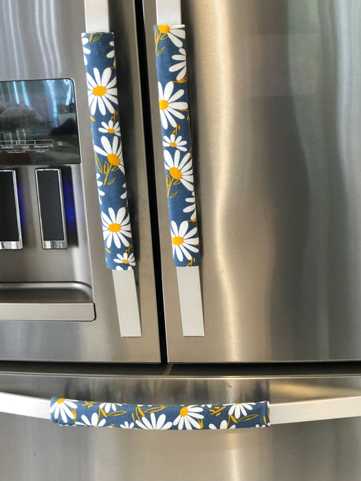 White and yellow daisy design on blue appliance handle covers for modern kitchen décor.