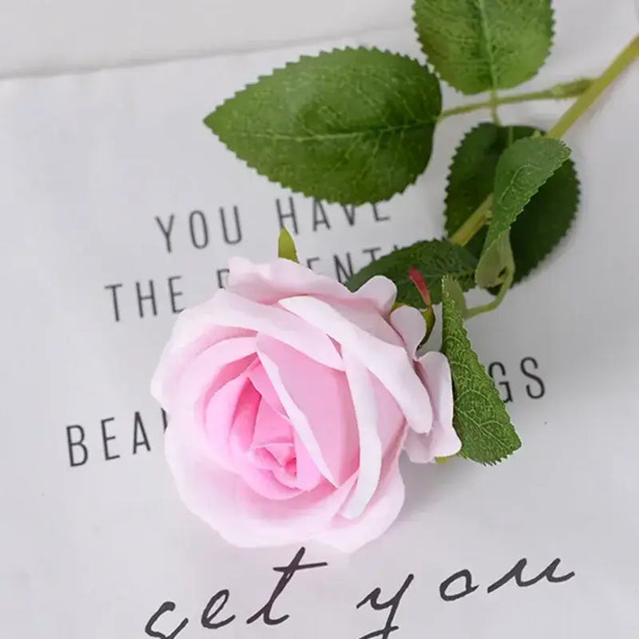 Artificial real-touch rose flower stems showcasing a lifelike pink rose with green leaves on a decorative background.