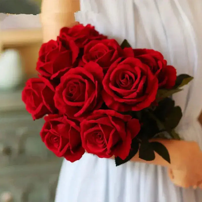 Artificial real-touch rose flower stems bouquet in vibrant red held by a person in a white dress.