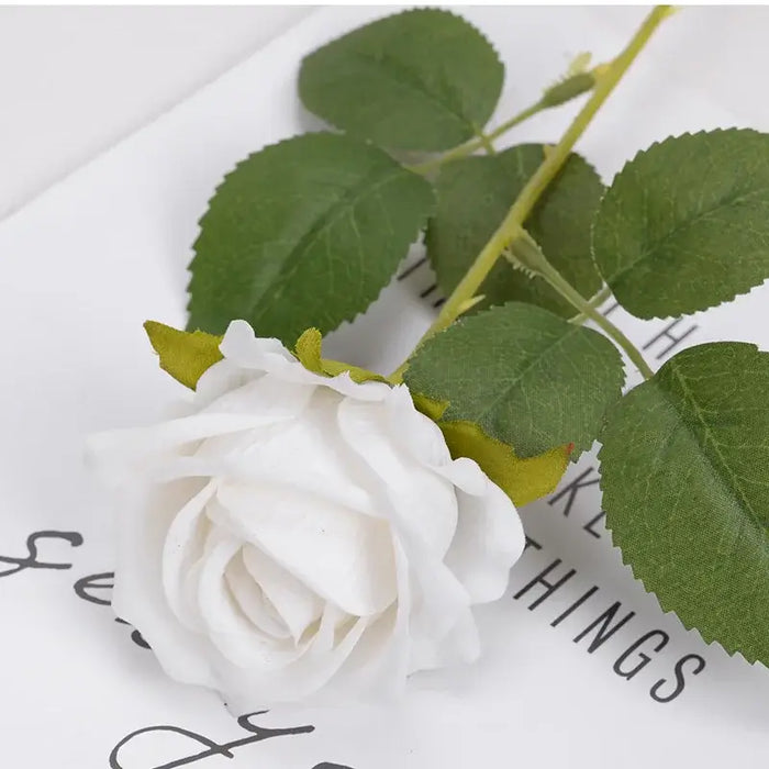 Artificial real-touch rose flower stems with white bloom and green leaves on a decorative surface.