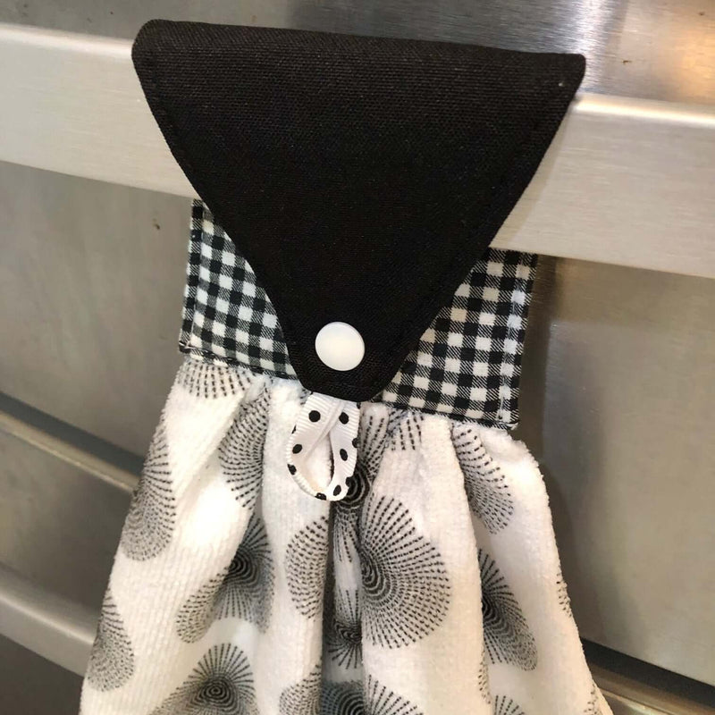 Black and white microfiber hanging hand towel with a checkered handle attached to a metal surface